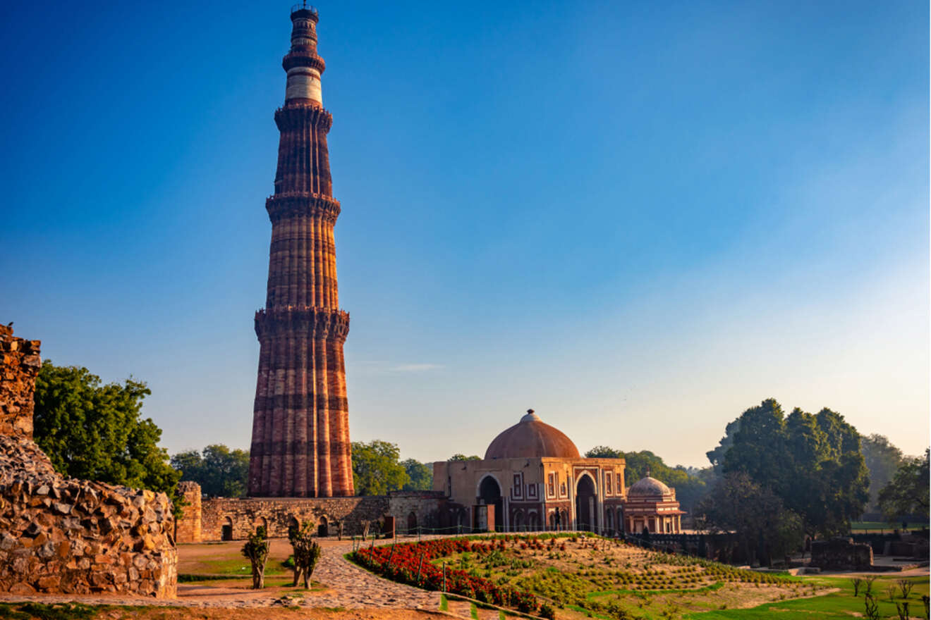 The Qutub Minar, a tall red sandstone tower, with a nearby historical structure, under a clear blue sky.