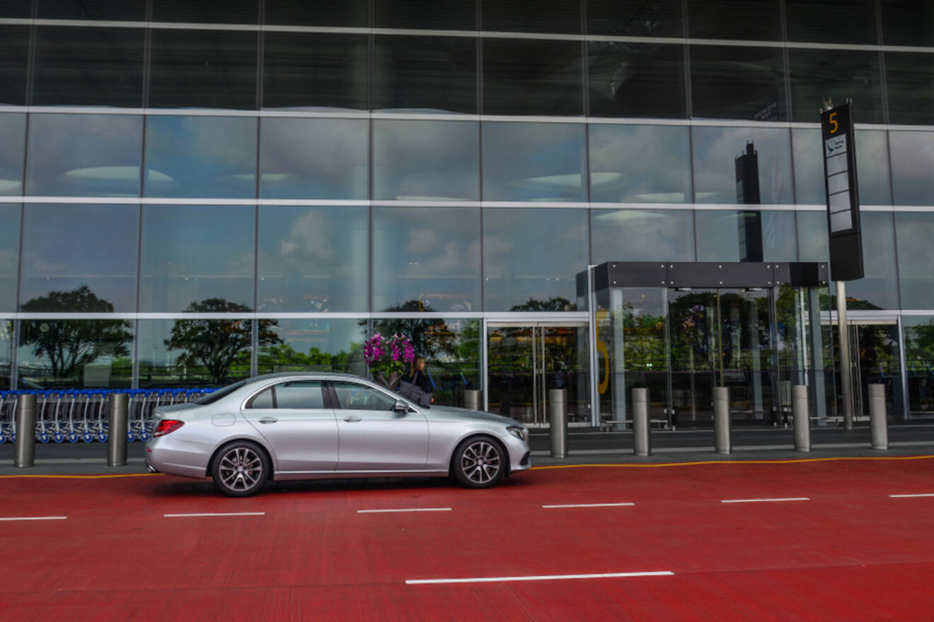 A silver car is parked in front of a modern building with glass windows and a red sidewalk.