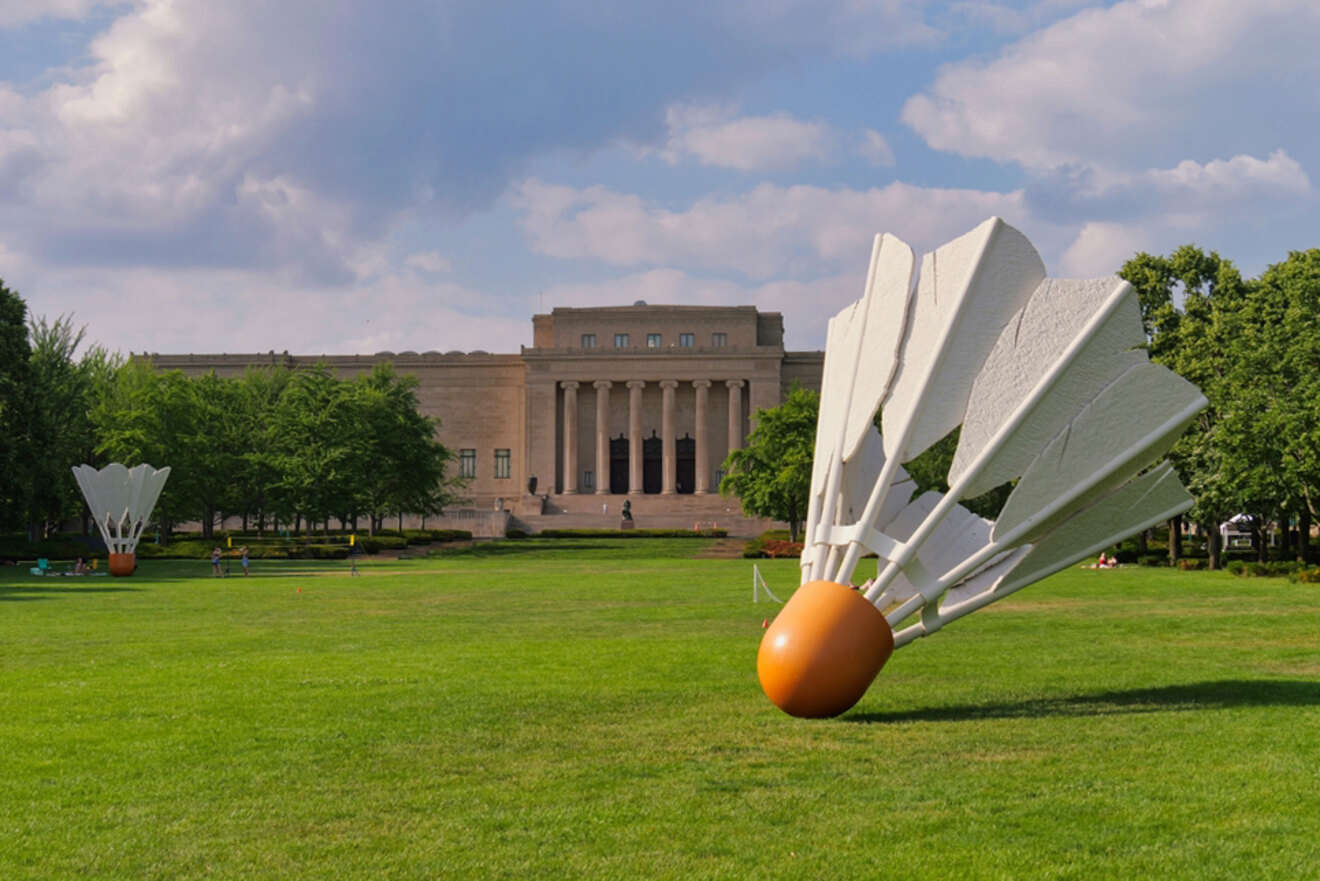 The Nelson-Atkins Museum of Art in Kansas City, with large shuttlecock sculptures in the foreground and a wide, green lawn leading to the museum's neoclassical facade.