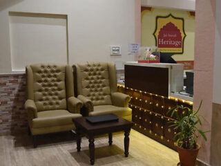 Two tufted armchairs and a small wooden table in a reception area. The wall behind features a sign reading "Heritage," and a potted plant is positioned beside the reception desk.