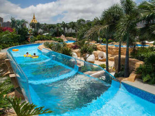 Water park at Broadway Hotel with a clear tube water slide winding through tropical palm trees and pools