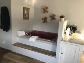 A bathroom features a red bathtub with folded white towels, coastal decorations on the wall, and a nearby countertop with toiletries and a potted plant.