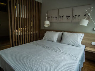 A neatly made bed in a modern room with wooden accents. Wall art with bird silhouettes hangs above the headboard. Two adjustable lamps are mounted on each side.