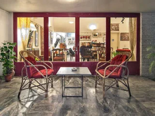 A seating area with two wicker chairs and a small table in front of a glass window showing an indoor lounge.