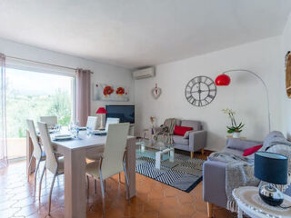 A cozy living room with a dining area, featuring a large clock, modern furniture, and a vibrant red floor lamp