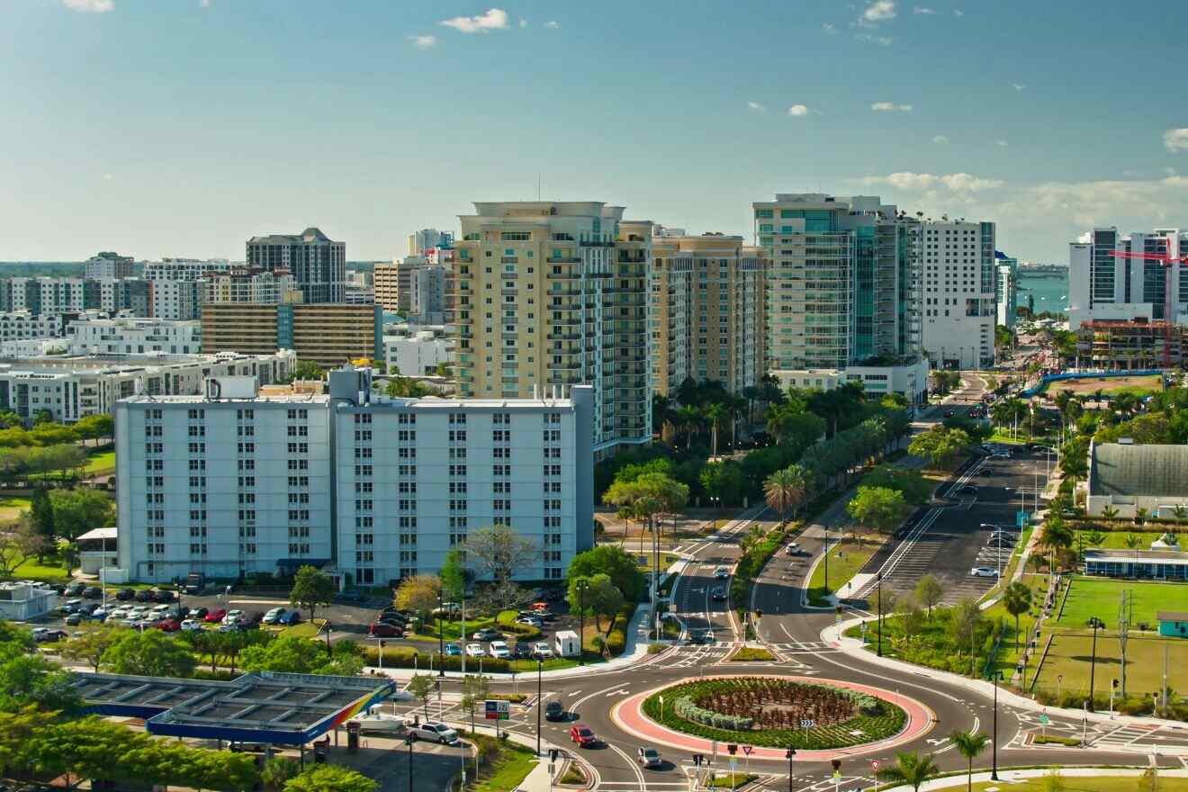 A cityscape view of the Rosemary District in Sarasota, featuring mid-rise residential buildings, palm trees, and a central roundabout, all under a clear sky.