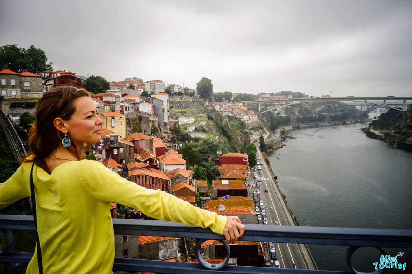 The writer of the post in a yellow shirt stands on a bridge overlooking a river and the vibrant cityscape of Portugal, with colorful buildings and a distant bridge.