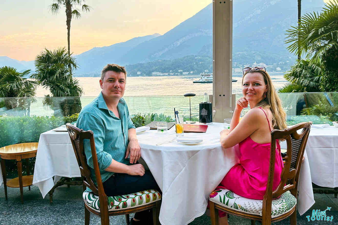 author of the post with husband sitting at an outdoor restaurant table with a lake and mountain scenery in the background.