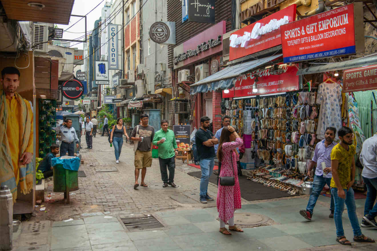 A bustling street in Khan Market, New Delhi, with shops, people walking, and vendors displaying their goods.