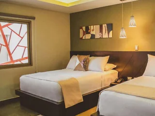 A hotel room with two neatly made double beds, contemporary decor, pendant lighting, and a window with a modern art design.