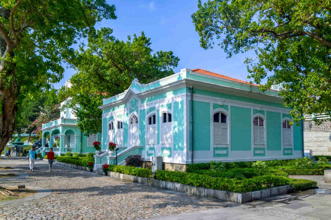 Taipa Houses Museum in Macau, showcasing a row of colonial-era pastel green buildings surrounded by trees and cobblestone pathways under a sunny sky.