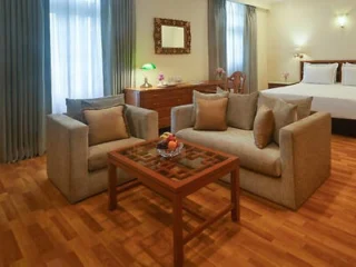 A luxurious hotel suite with a sitting area, coffee table, and bed, decorated in neutral tones.