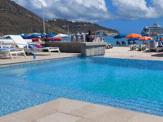 A beachside pool area with white lounge chairs and colorful umbrellas, set against a backdrop of mountains