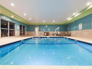 Indoor swimming pool in a hotel, featuring bright lighting and blue water, with tables and chairs