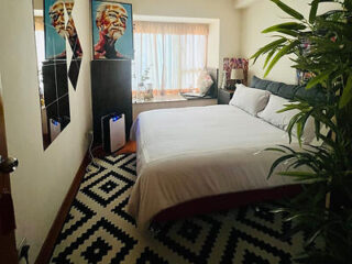 A small bedroom in Taipa featuring a neatly made bed with white sheets, patterned black and white carpet