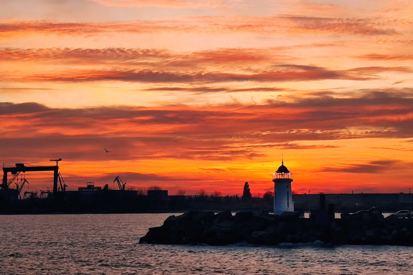 Colorful sunset over a coastal lighthouse, with an industrial backdrop and calm water in the Cook Islands.