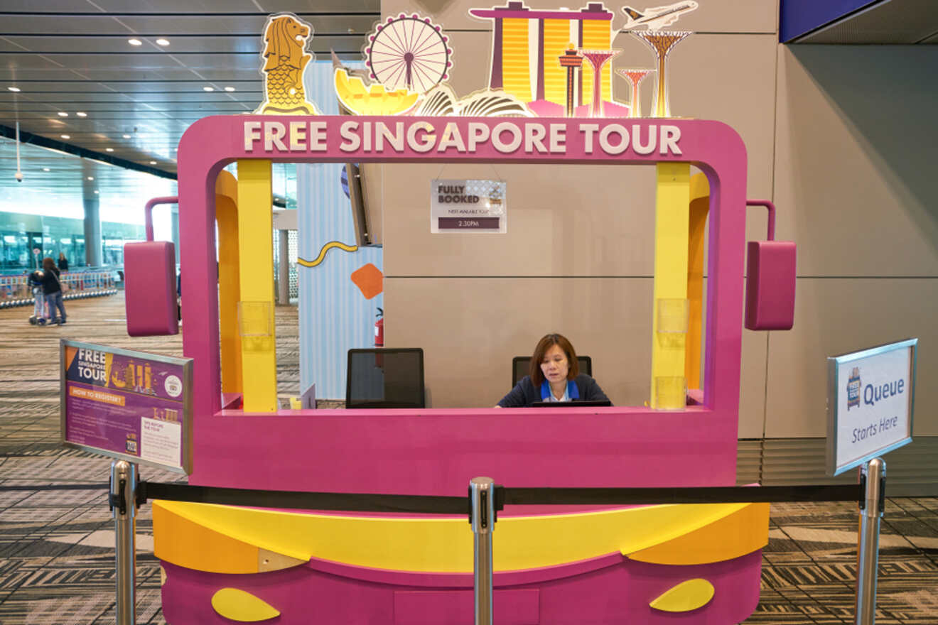 A woman is seated at a "Free Singapore Tour" booth inside an airport. The "Fully Booked" sign is displayed, and there's a "Queue Starts Here" sign to the right.