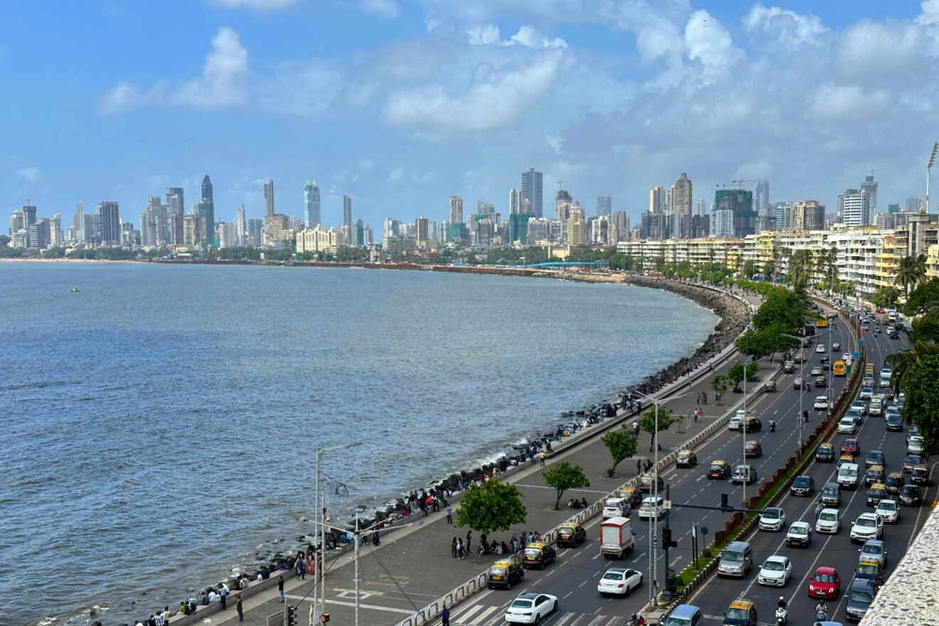 A coastal cityscape view showing a busy road along the waterfront with high-rise buildings in the background under a partly cloudy sky.