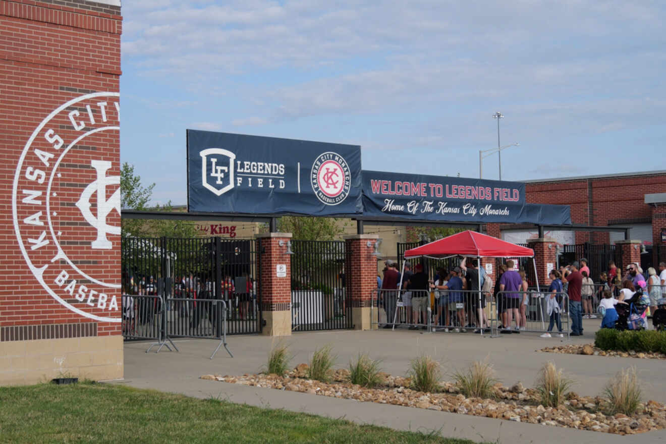 Entrance to Legends Field in Kansas City, with a sign welcoming visitors and people lining up at the gates under a red tent.