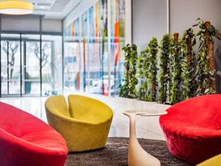 A modern lobby with colorful, curved seats, a small white table, plants along the wall, and large windows showcasing an outdoor view.