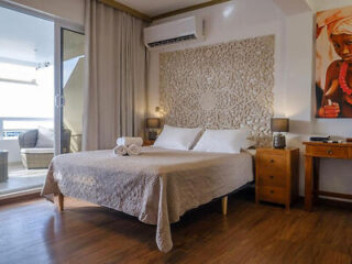 A stylish bedroom featuring a large bed with beige linens, a decorative carved headboard, and a sliding door leading to a balcony.