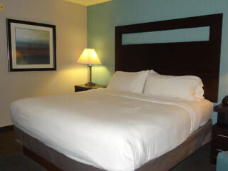 Hotel room with a large bed and simple decor, featuring a framed artwork on the wall and a lamp