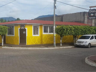 A yellow building with a red roof stands on a corner; a white van is parked on the street nearby.