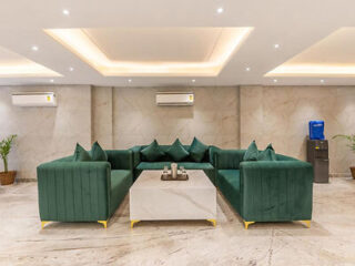 A modern lounge area with green sofas, a marble coffee table, and recessed lighting in the ceiling.