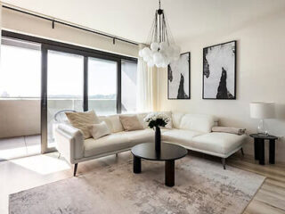 Modern living room with a white sectional sofa, round black coffee table, contemporary chandelier, abstract wall art, and large sliding glass doors leading to a balcony.