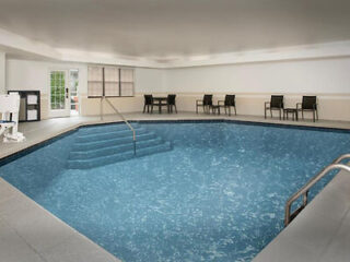 Indoor pool with stairs leading into the water, surrounded by chairs and tables