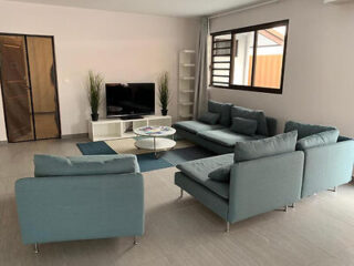 A spacious living room with a modern, light blue sectional sofa, a flat-screen TV, and a large window letting in natural light.