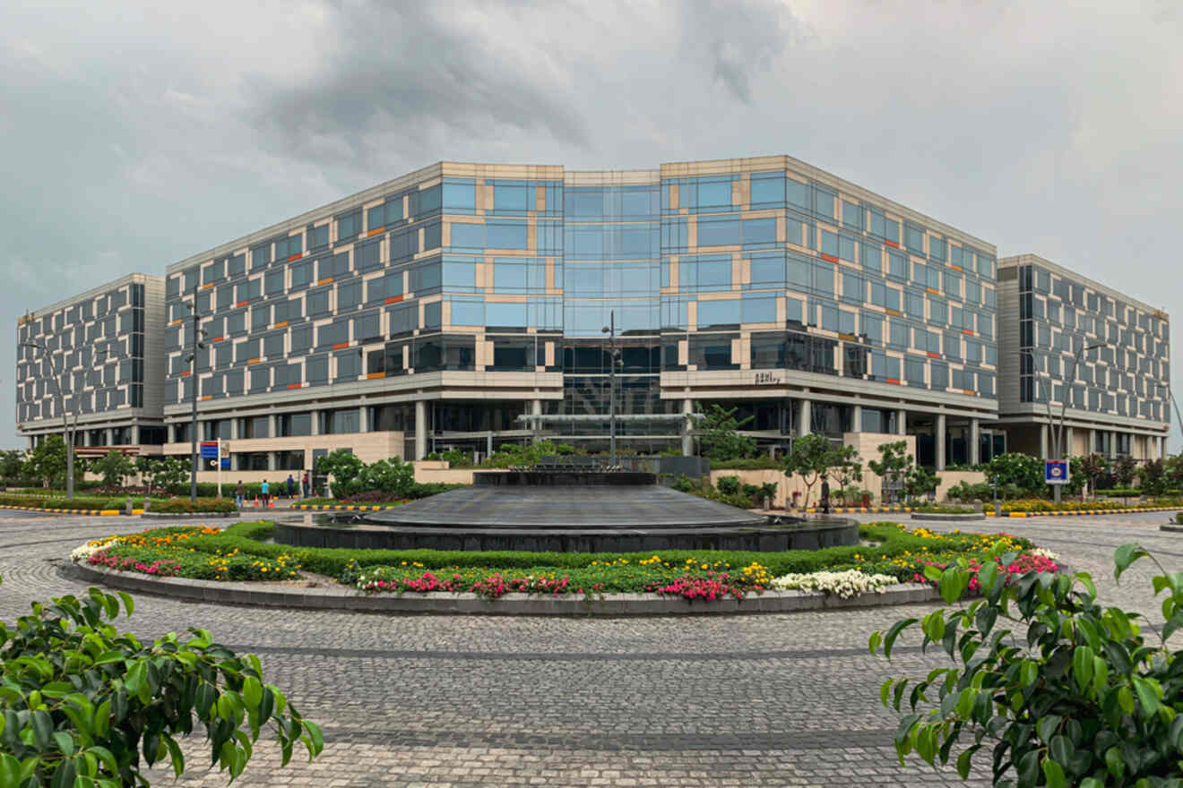 A modern glass-fronted building in Aerocity, New Delhi, surrounded by a landscaped garden and a circular driveway.