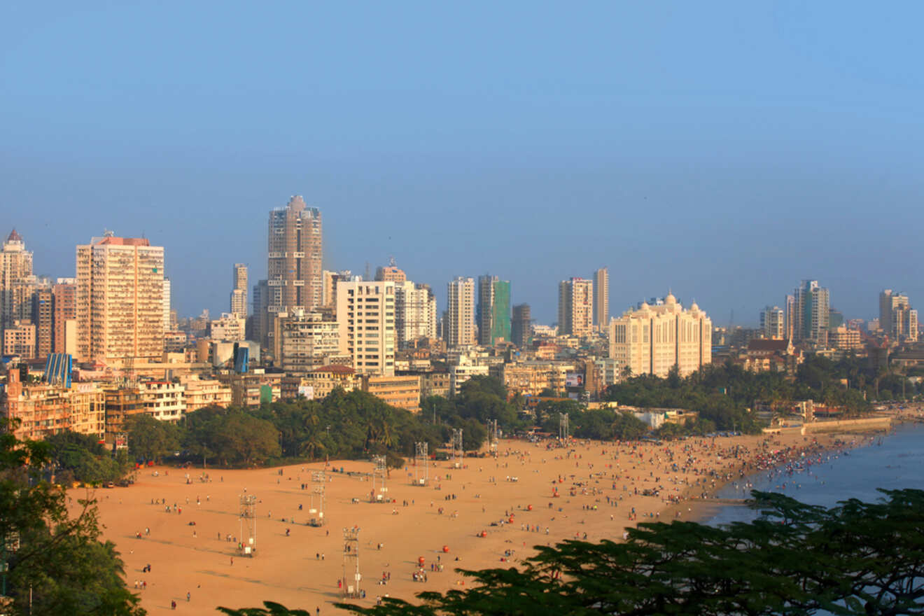 A wide sandy beach with people scattered across it, located next to a city with multiple high-rise buildings under a clear blue sky.