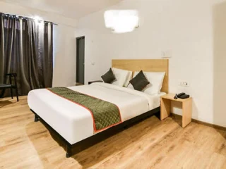 A modern hotel room with a large bed, wooden flooring, and minimalist decor.