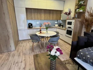 A modern kitchen and dining area with wooden floors, white cabinets, a round dining table with four chairs, floral centerpieces on the table and coffee table, and built-in appliances.