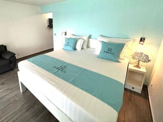 A bright bedroom with a large bed dressed in white linens and light blue accents