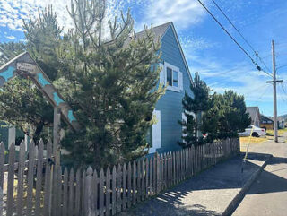 A blue house surrounded by trees with a wooden picket fence in front. The clear sky and a parked car are visible in the background.