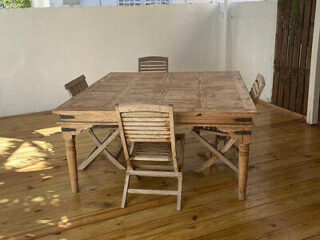 A simple outdoor wooden dining table and chairs set on a polished wooden deck