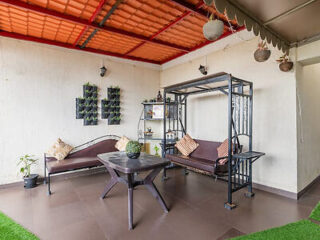 Covered outdoor patio with a red-tiled roof, featuring two metal sofas with cushions, a small table, wall decor, and some plants.