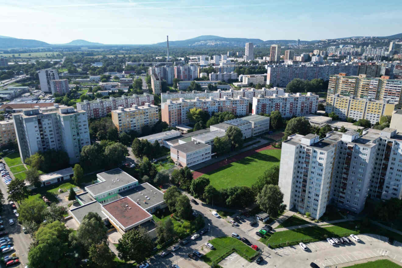 Aerial view of a residential area with multiple high-rise apartment buildings, green spaces, and distant hills under a clear sky.