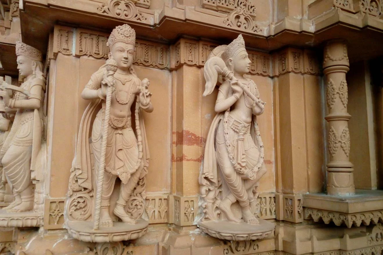 Ornate stone carvings depicting two figures in traditional attire, part of a larger architectural structure, with intricate detailing and decorative elements surrounding the figures.