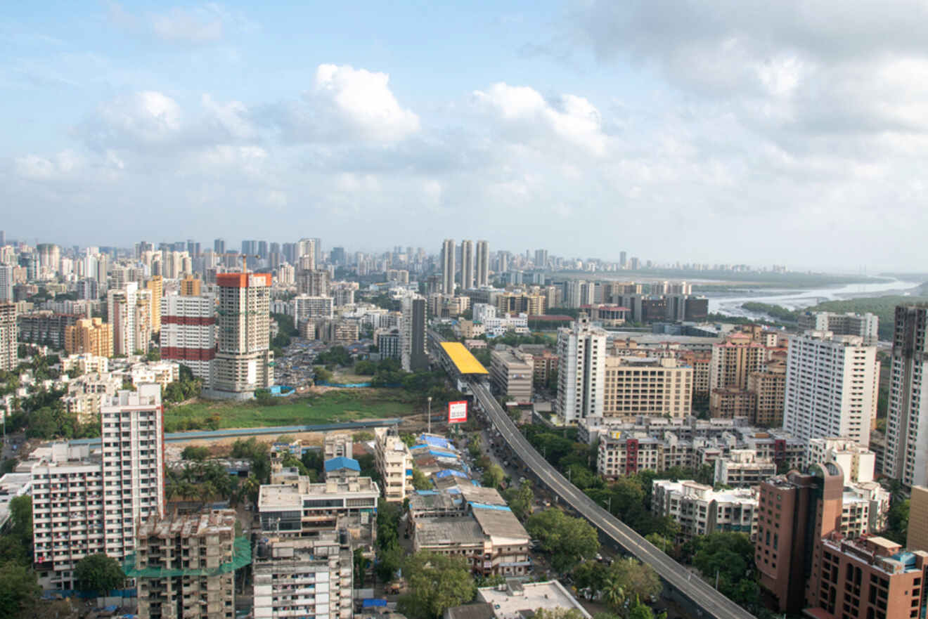 Aerial view of a cityscape featuring numerous mid and high-rise buildings, a central highway, and a river in the background under a cloudy sky.