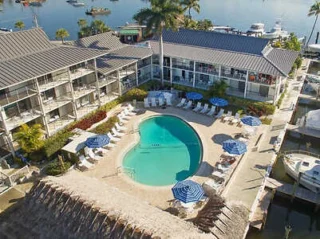 Aerial view of a resort with a heart-shaped pool, surrounded by lounge chairs and blue umbrellas, near a marina with boats.