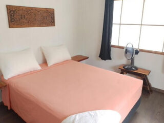 A cozy bedroom with a pink bedspread, a wooden fan on the side, and tropical-style decor.