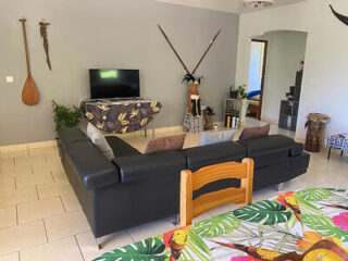 A living room decorated with traditional Polynesian accents, featuring a large black leather sectional and a flat-screen TV.