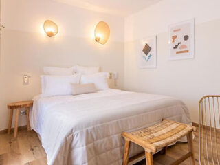 A bright, minimalist bedroom with white walls, a neatly made bed with soft lighting