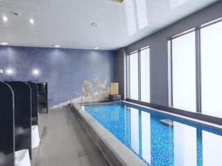 Indoor swimming pool with blue tiles, located next to a wall featuring a nautical mural. The pool is positioned beside a row of black changing stalls and a set of large windows.