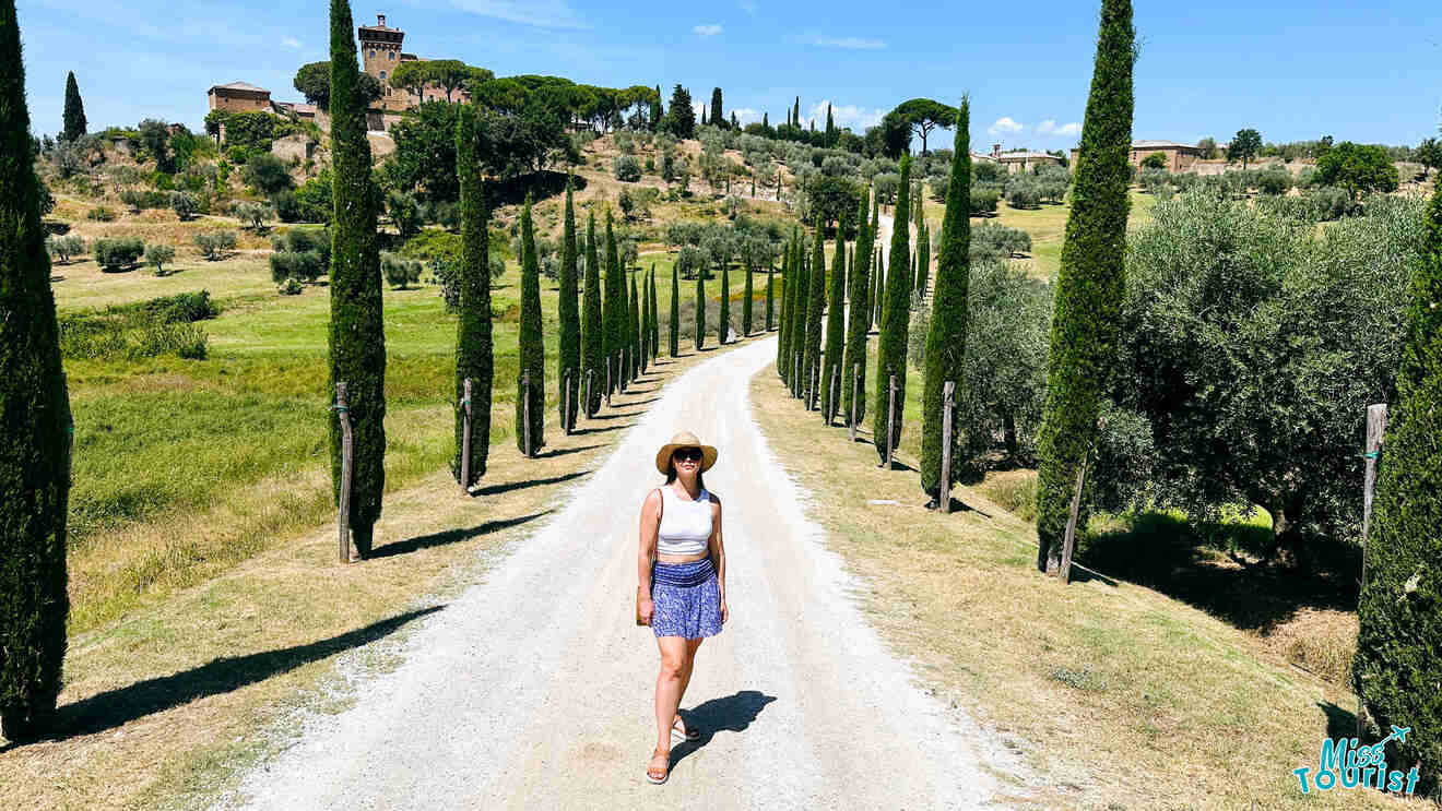 The writer of the post walks down a gravel driveway lined with tall, narrow cypress trees, leading towards a distant Tuscan villa