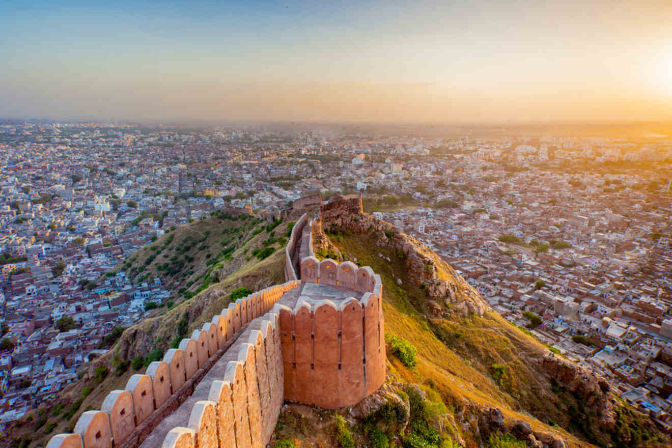 Panoramic view of a cityscape at sunset with an old, fort-like wall extending along a hill in the foreground.