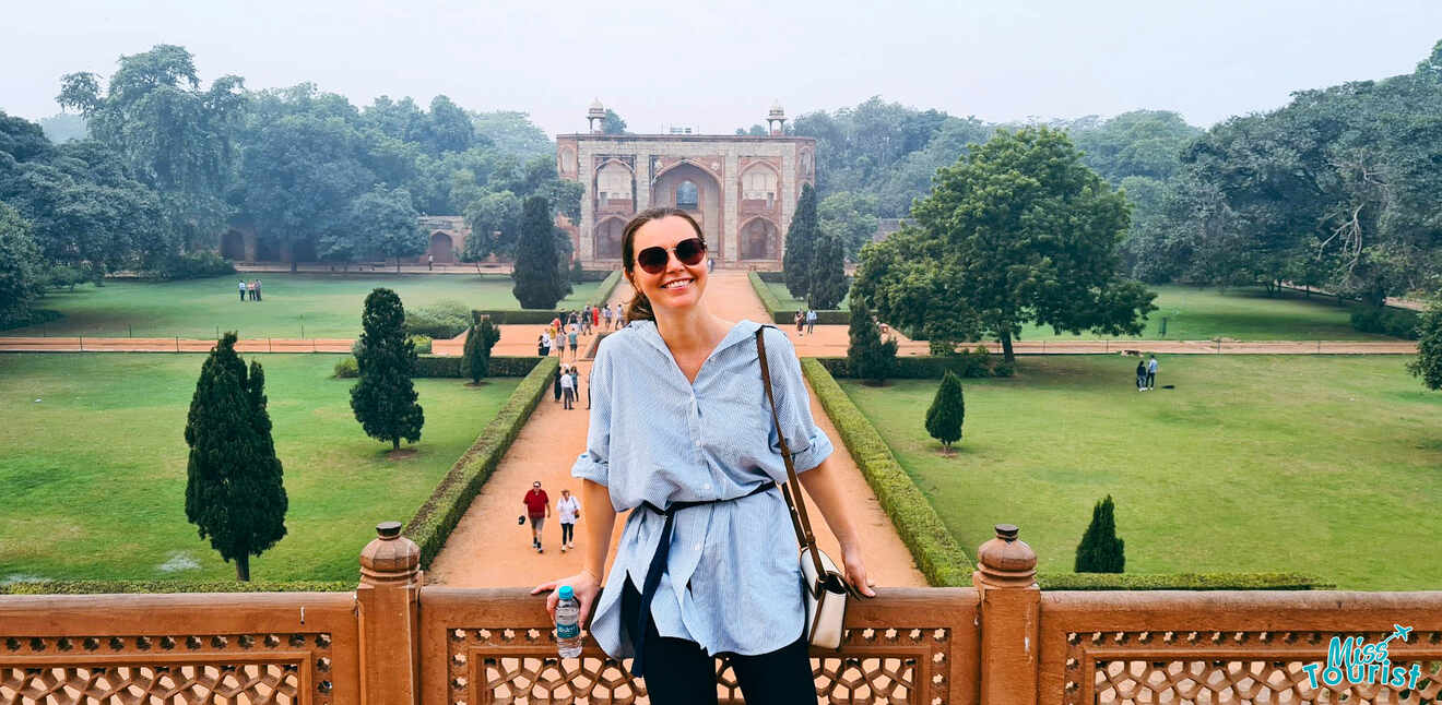 The writer of the post standing in front of Humayun's Tomb, smiling, with lush gardens and trees in the background.